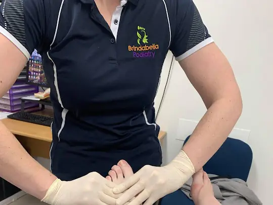 A Brindabella Podiatry podiatrist in gloves holds a patient's bare foot during treatment