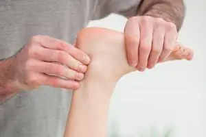 A practitioner's hands hold a patient's foot and press on the back of the heel