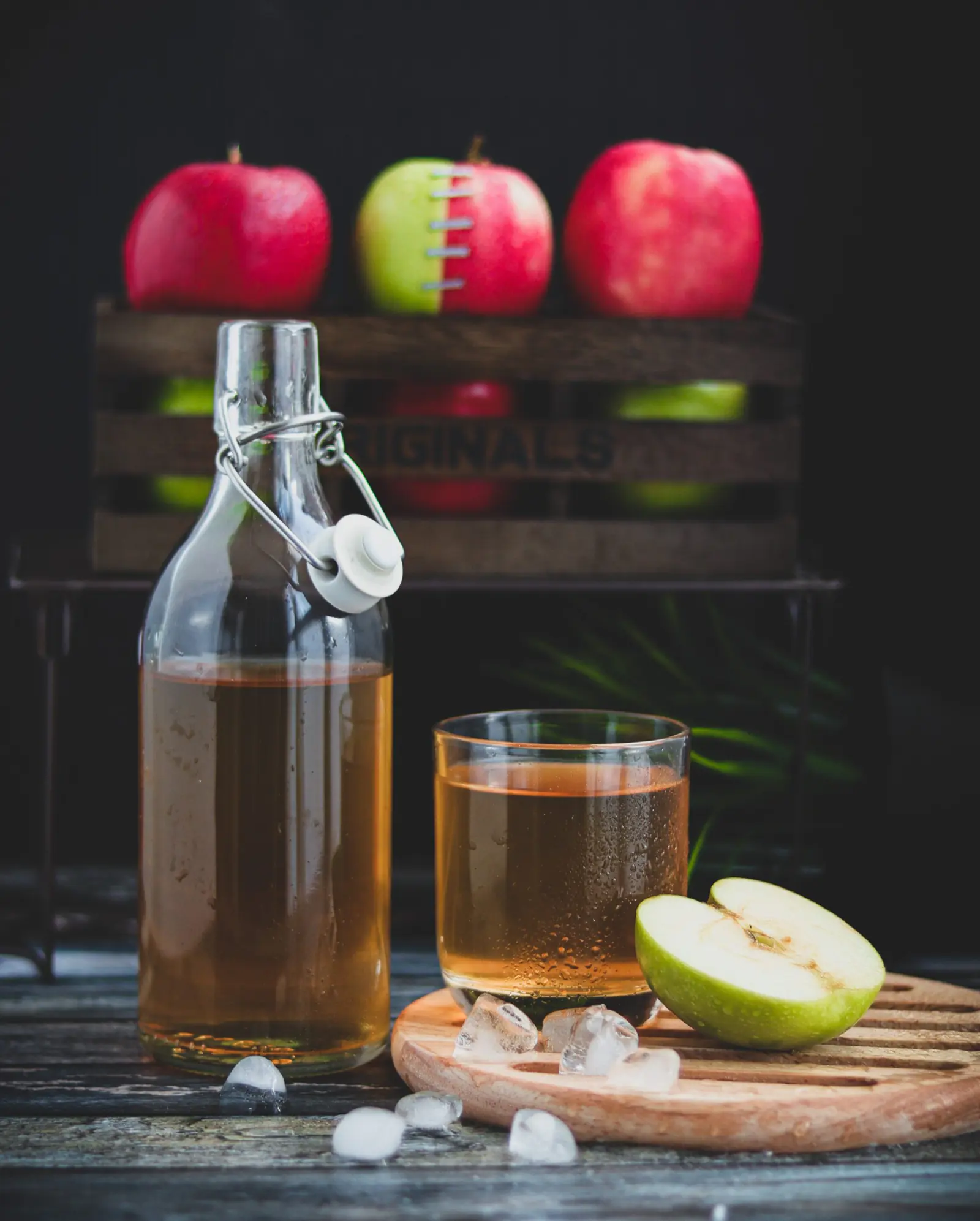 A bottle and a glass of apple cider vinegar with fresh red and green apples