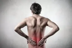 A man holds his lower back, with the painful area shaded red