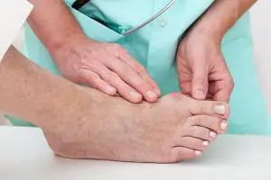 A clinician in scrubs examines the top of a patient's bare foot