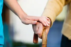A carer's hand rests on an older person's hand as they hold a walking stick