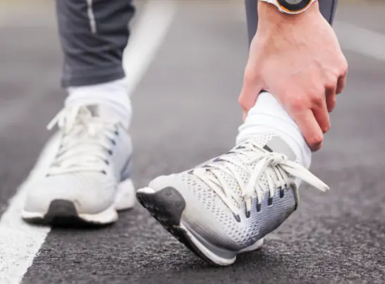 A runner in grey sneakers holds their ankle on the road