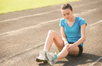 A young woman sits on a running track and holds her knee