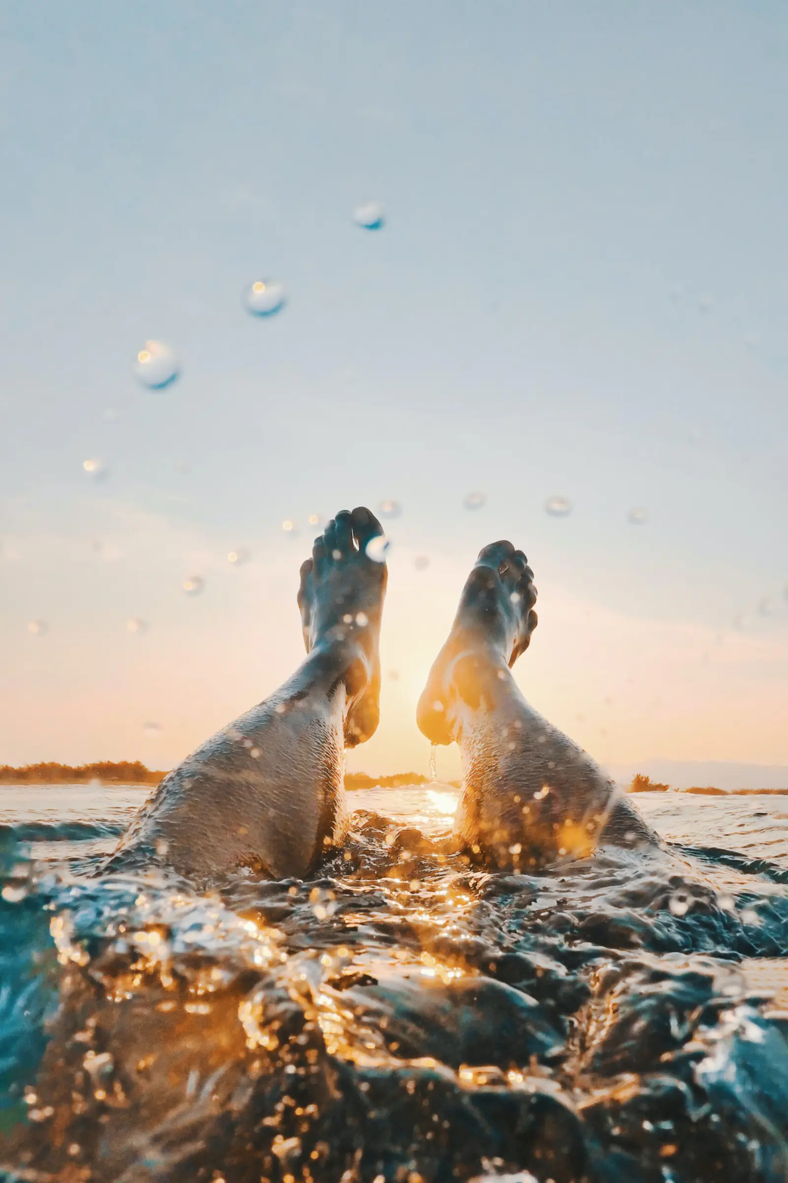 Bare feet raised out of splashing water at sunset