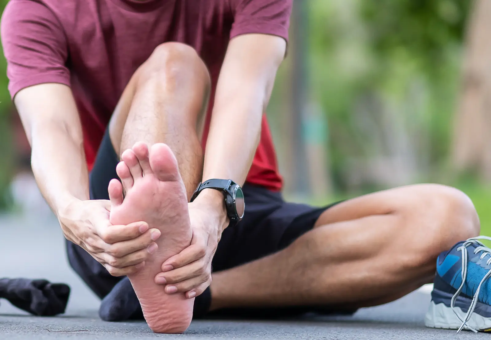 A runner sits on a path and holds the sole of his bare foot