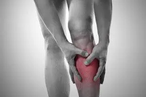 A person holds the front of their lower leg, with the shin shaded red
