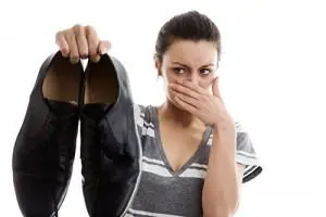 A woman holds up a pair of black shoes and covers her nose
