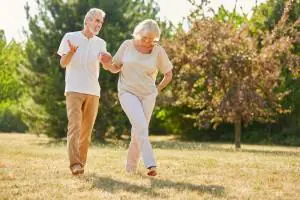 An older couple walk together across a grassy park